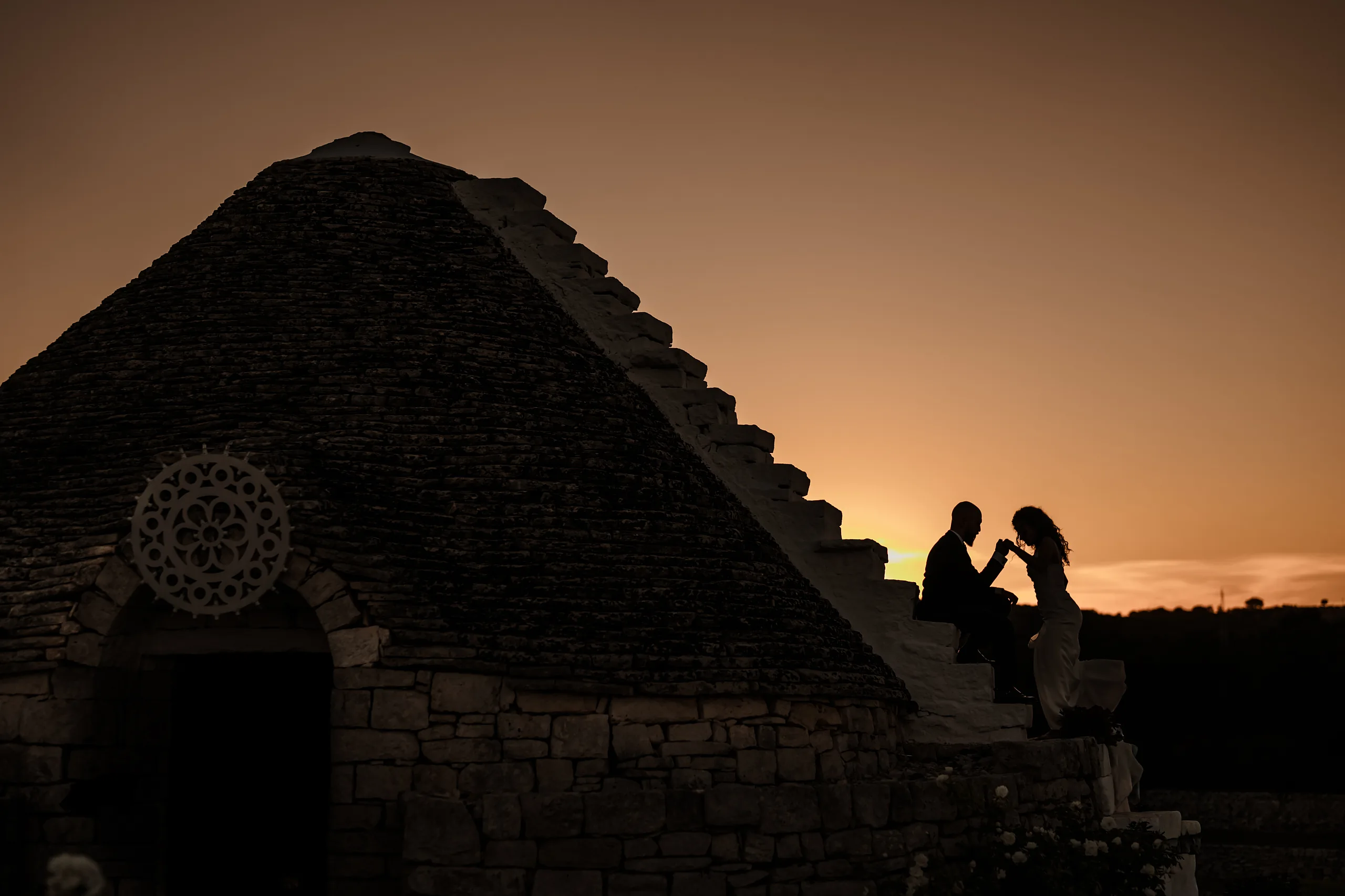 Sposi in silhouette davanti a una chiesa in pietra al tramonto in Puglia