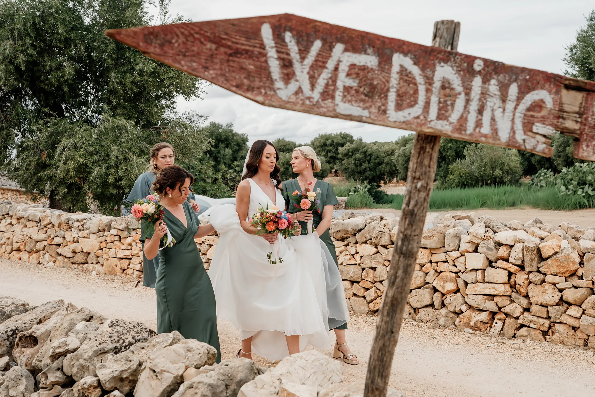 Damigelle e sposa accanto a un cartello Wedding tra i muretti a secco