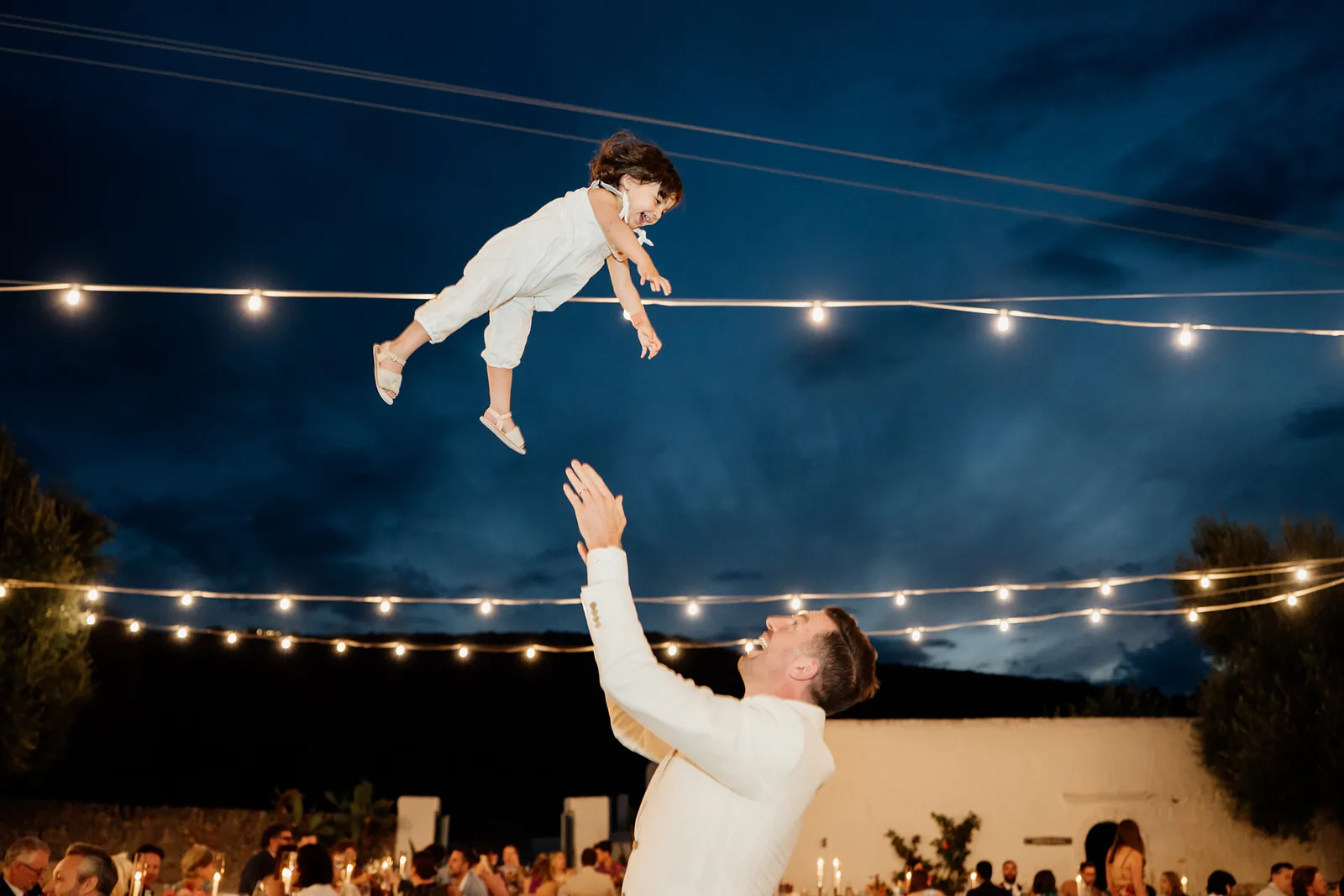 Bambino lanciato in aria sotto le luminarie del ricevimento