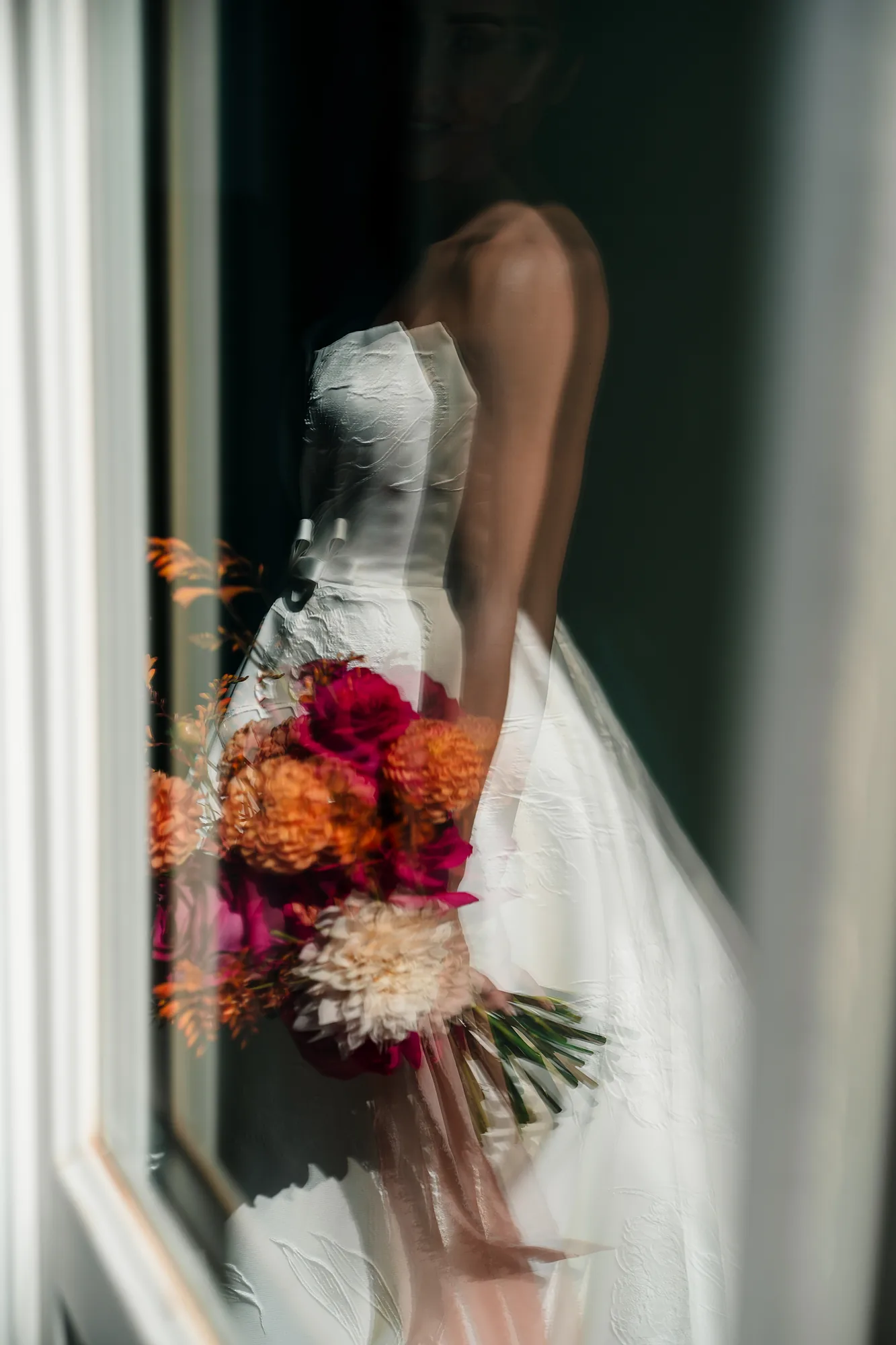 Sposa con bouquet colorato riflessa in una vetrata