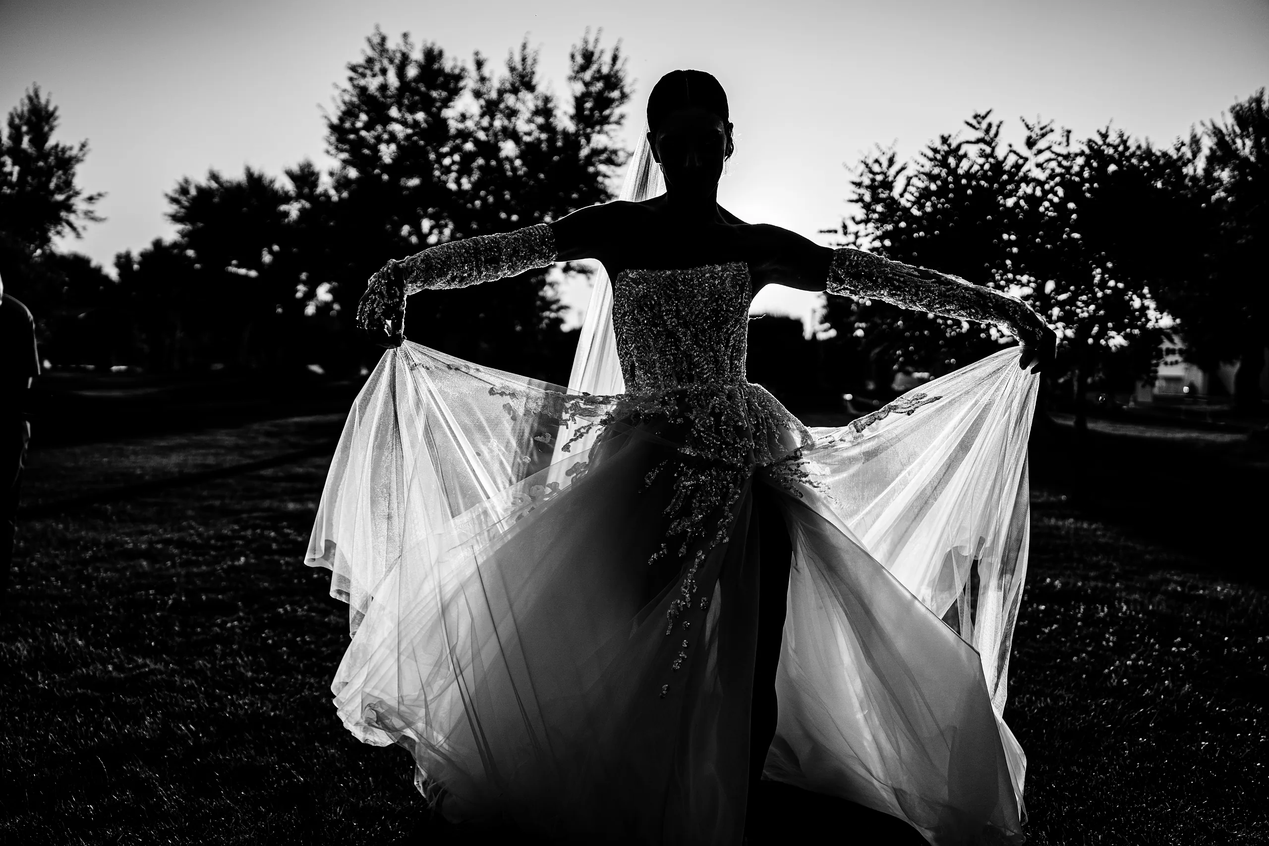 Sposa in controluce che apre l'abito, in bianco e nero