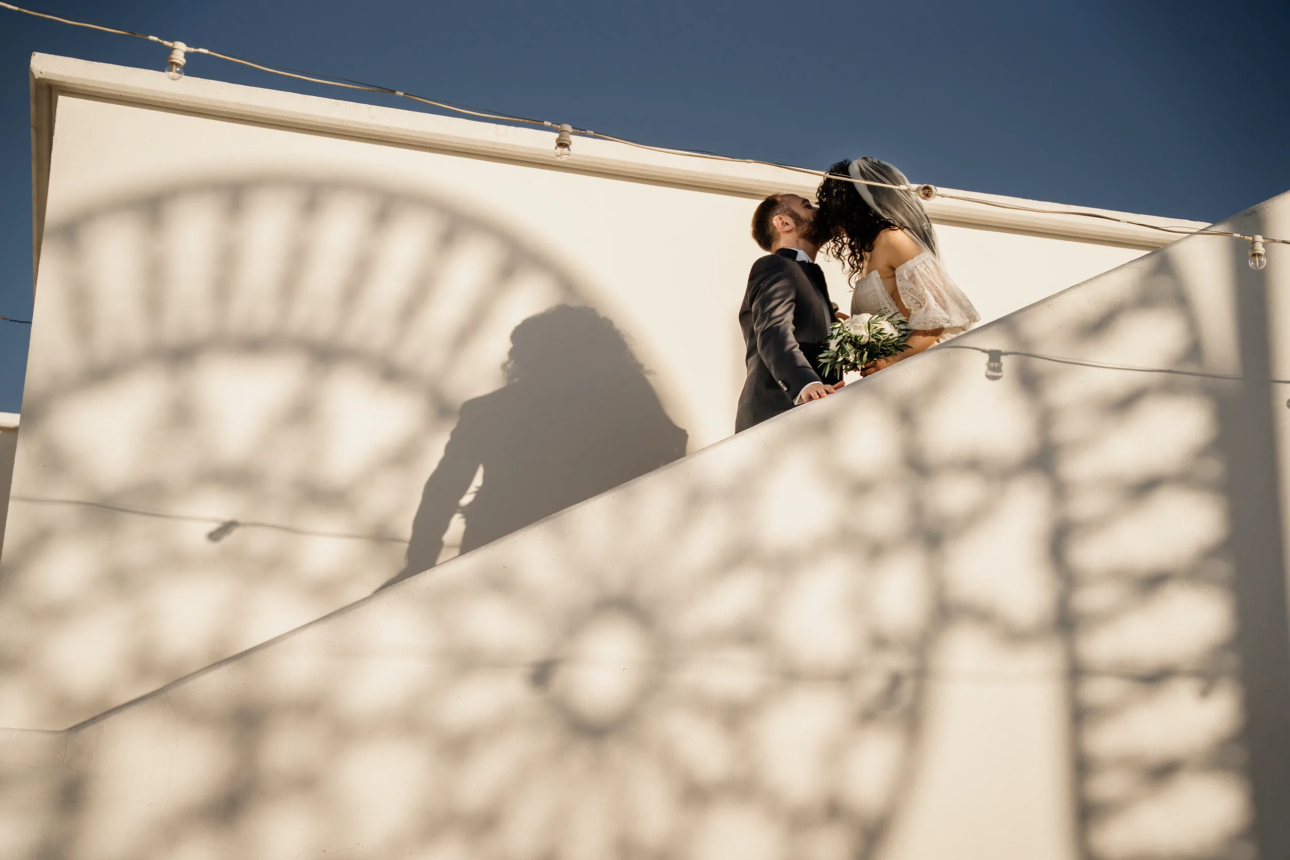 Sposi su una terrazza con l'ombra di un rosone proiettata sul muro