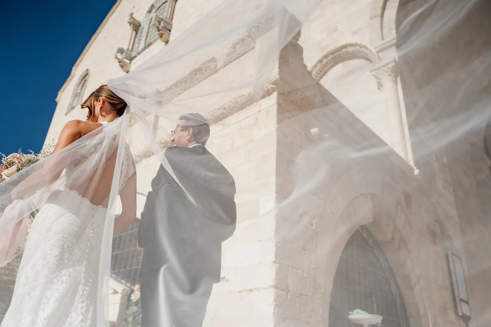 Il velo della sposa sollevato dal vento davanti alla facciata della chiesa